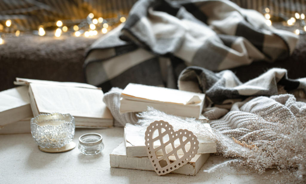 Cozy home decor with books, candle, soft blankets and warm fairy lights